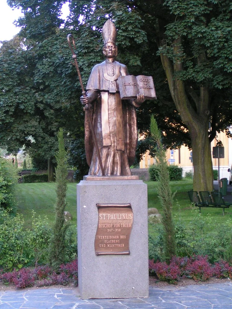 Фотография бронзового памятника с немецкой надписью «ST. PAULINUS BISCHOF VON TRIER 347-358 VERTEIDIGER DES GLAUBENS UND MÄRTYRER»